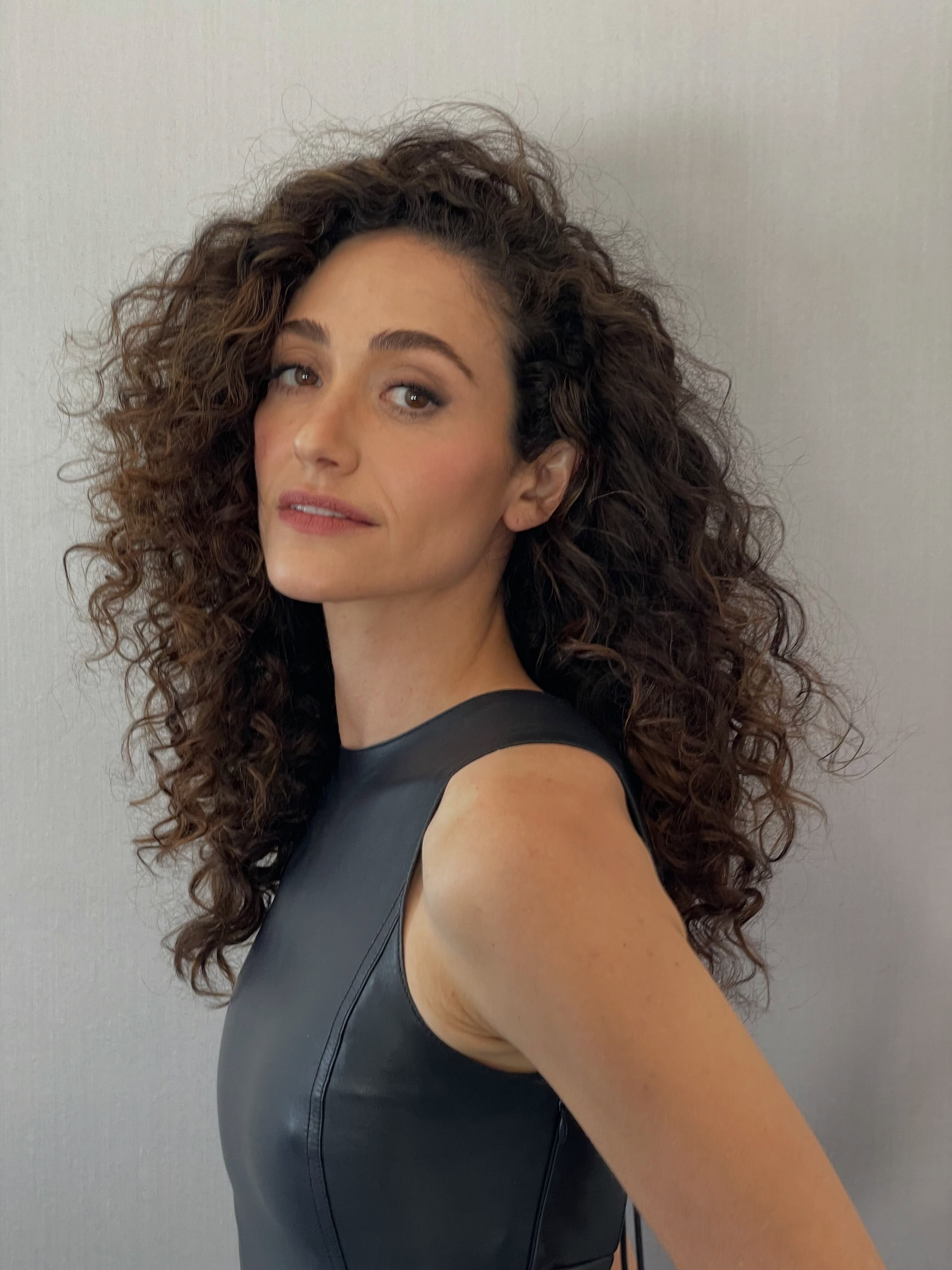 Portrait of Emmy Rossum from the chest up looking at the camera on a gray background